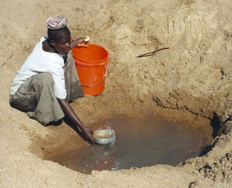 Mwamanongu Village water source, Tanzania. Water often comes from open holes dug in the sand of dry riverbeds, and it is invariably contaminated. Our research pointed to the importance of linking identifiable people to climate impacts. The concentration on this young woman's face, in order to access limited and possibly contaminated water, provides a personal window on how drought impacts people's lives.